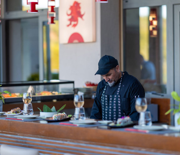 Sushi Bar chef cooking behind the decorated bar with food and glasses wine